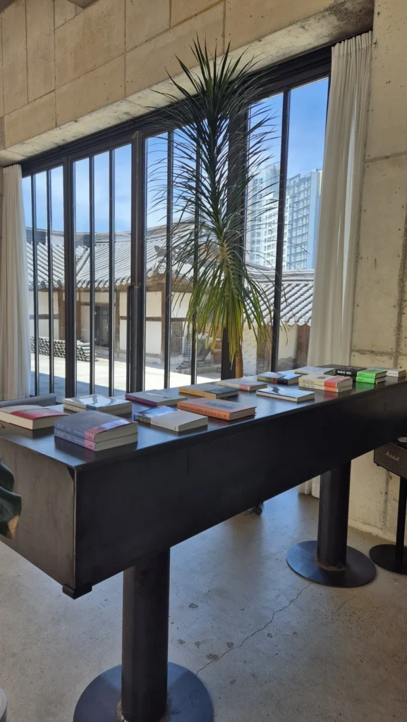 Steel reading table with books beside windows overlooking traditional hanok tiled roofs